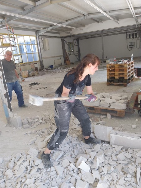 Esther Bartlog reißt mit dem Vorschlaghammer eine Wand in der Halle ab