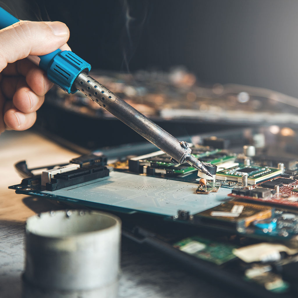 Hand mit Lötkolben bei der Reparatur einer Elektronikplatine
