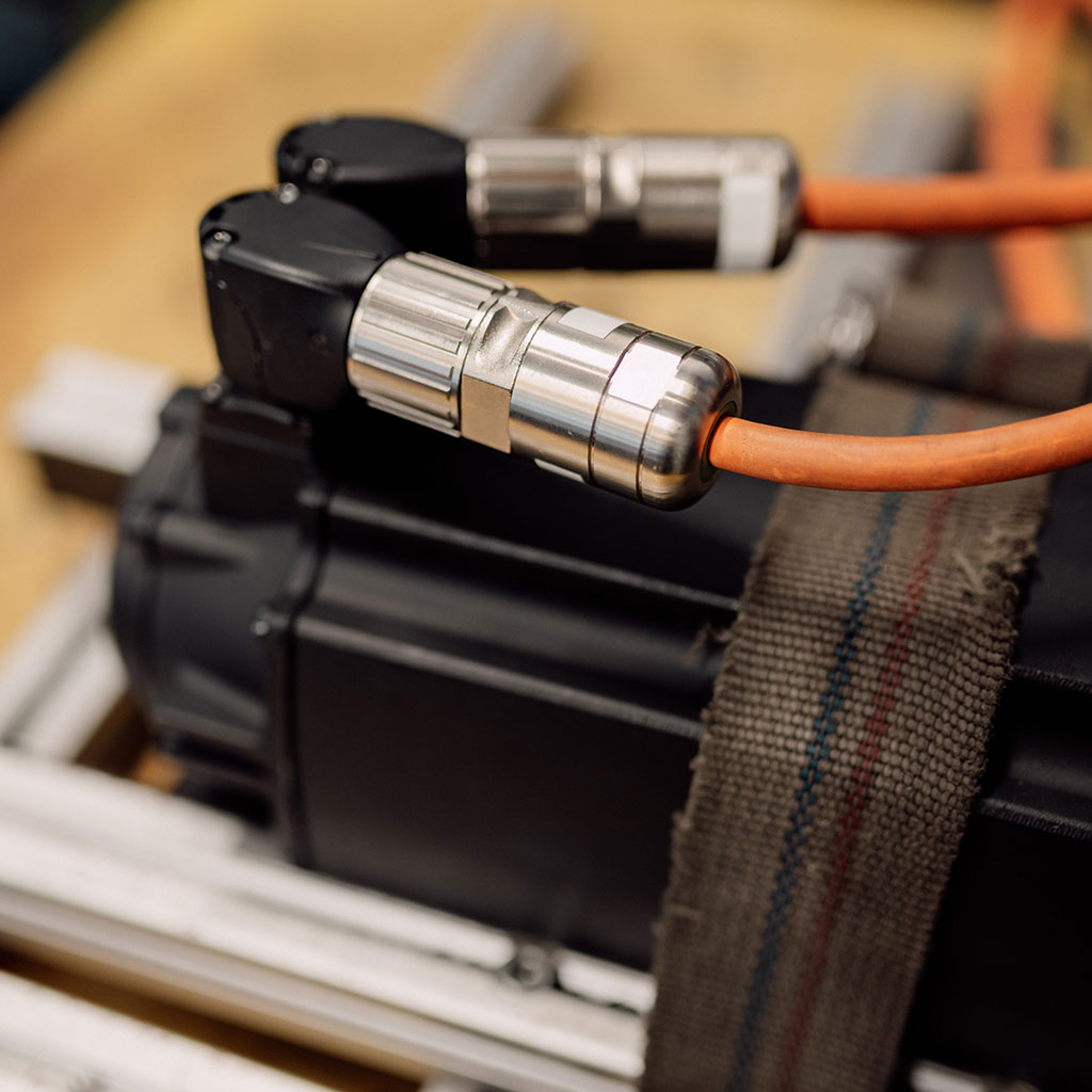 Servomotor mit zwei Rundsteckverbindern und orangen Kabeln auf dem Prüfstand